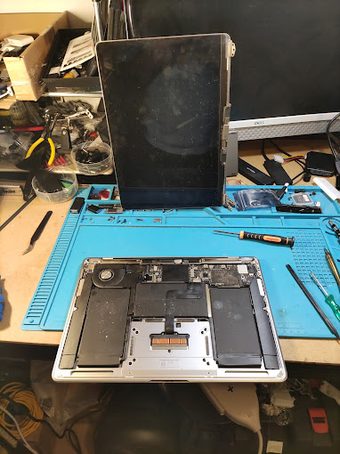 MacBook screen replacement in progress: old display panel removed and the bare chassis open on the workshop mat